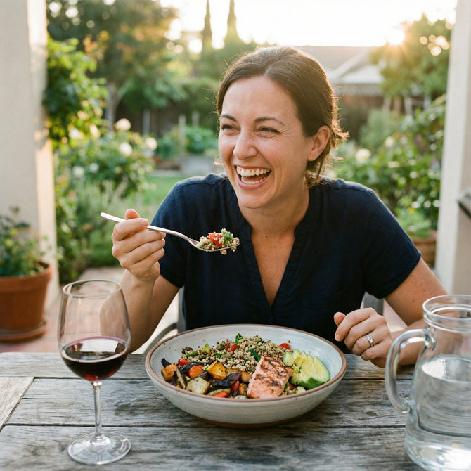 Woman enjoying a meal outdoors with a bowl of salad and glass of wine.