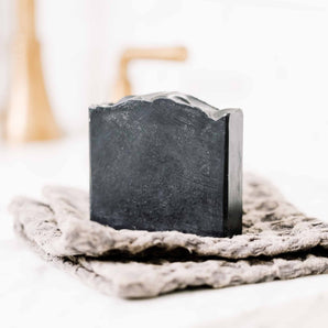 Handmade charcoal bar soap with tallow and goat milk by Pretty Farm Girl, showing a dark, textured soap bar on a natural surface.